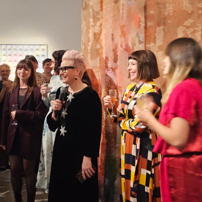 Exhibition opening at Curatrial+Co. gallery with Sophie Vander, Director holding a microphone.